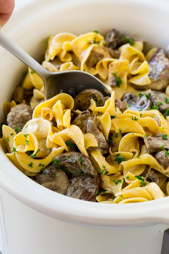 Slow Cooker Beef Stroganoff Recipe | Crock Pot Beef Stroganoff | Beef Recipe #slowcooker #crockpot #beef #mushrooms #pasta #dinner #dinneratthezoo A crock pot of beef stroganoff with a serving spoon in it.